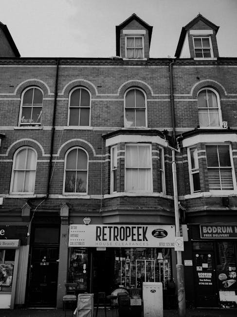 A black-and-white photograph depicts a busy street scene outside a pharmacy and shopfronts on Tottenham High Road. In the foreground, a variety of discarded furniture and household items are lined up 